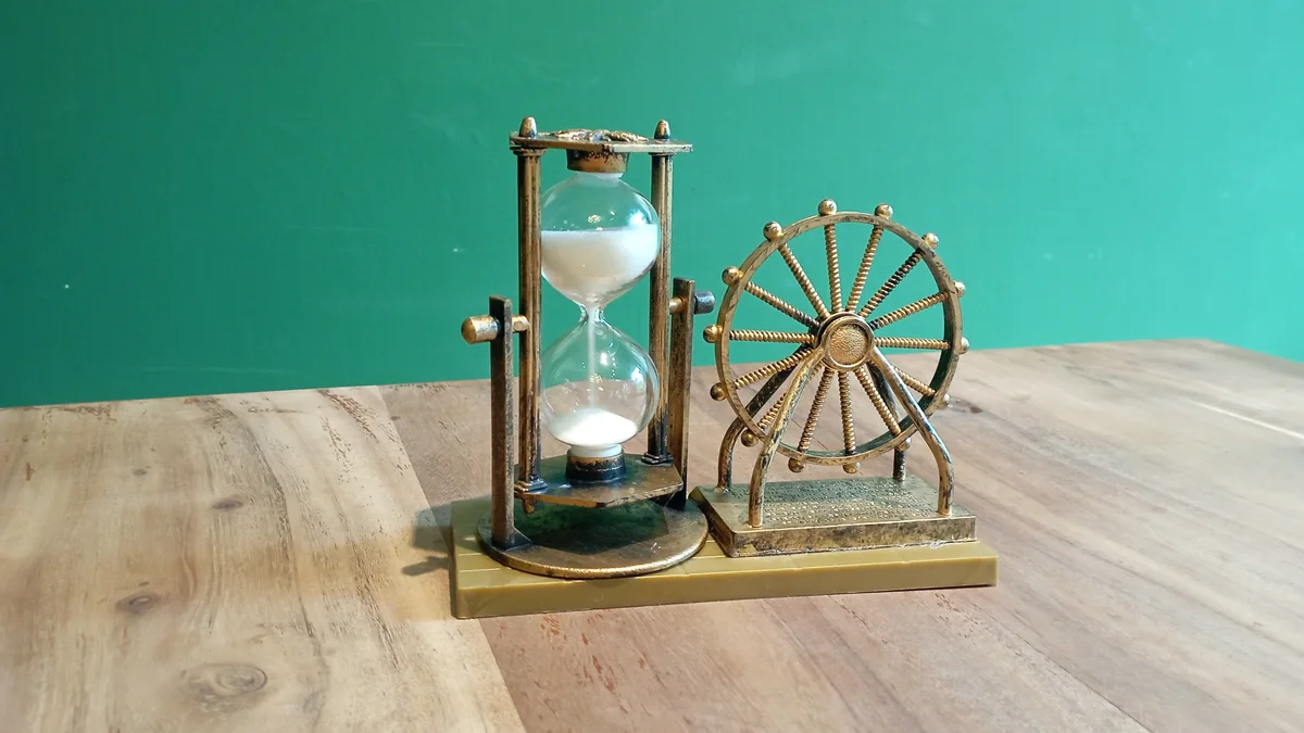 Sanduhr mit weißem Sand neben einem kleinen Riesenrad aus Metall auf einem Holztisch