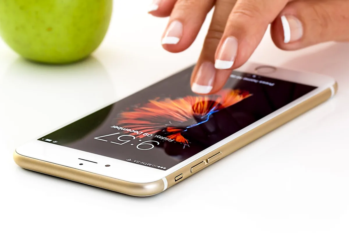 Finger tippt auf den Bildschirm eines Smartphones, daneben ein grüner Apfel
